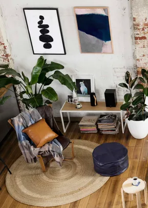 Cozy living room with plants, a leather chair with pillows, abstract wall art, and a small white table with decor.