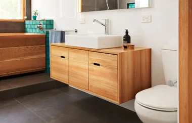 Modern bathroom with wooden vanity, white sink, and teal tile accents.
