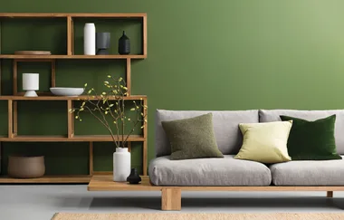 Modern living room with green wall, wooden shelves, gray sofa, and decorative cushions and vases.