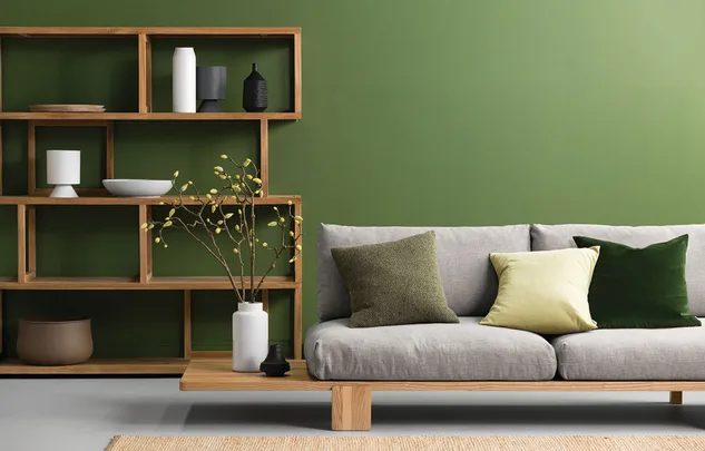 Modern living room with green wall, wooden shelves, gray sofa, and decorative cushions and vases.