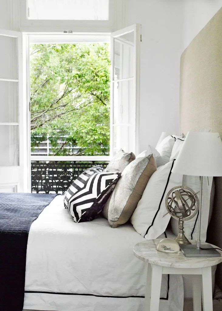 A white and black bed with decorative cushions in good bedroom feng shui positioning to the door