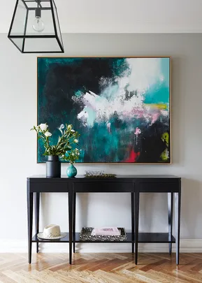 Elegant console table with floral decor and abstract painting on wall.