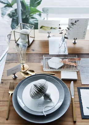 Elegant table setting with gray plates, gold utensils, a glass, and a paper shell decoration on a wooden surface.