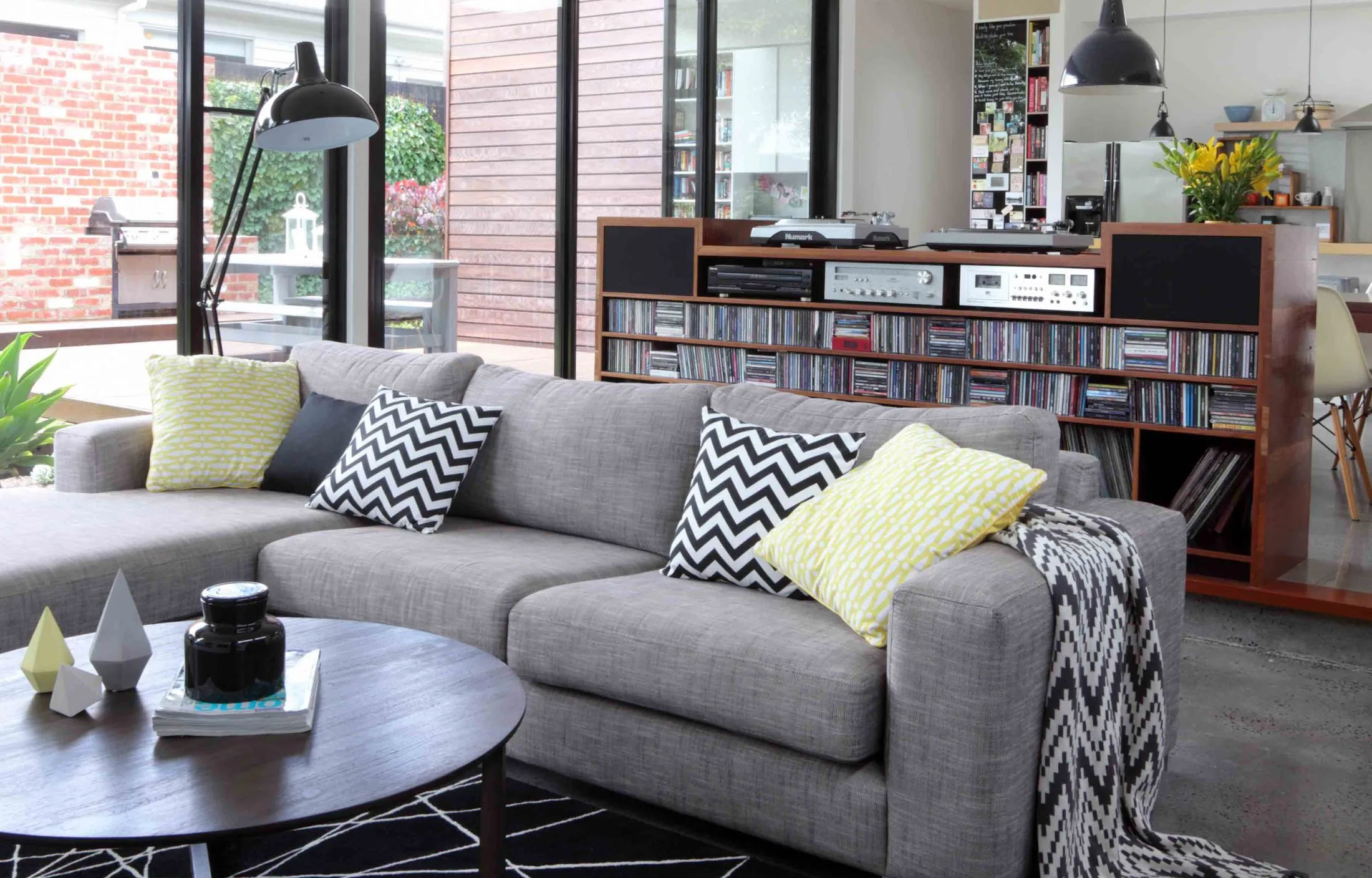 Living room with gray sofa, chevron cushions, a coffee table, and a shelf with books and audio equipment.