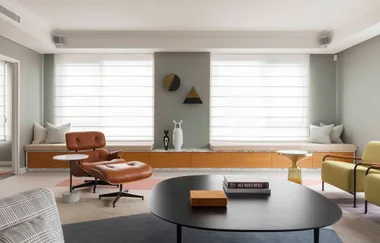 Modern living room with a brown leather chair, books on black coffee table, and large windows with blinds.
