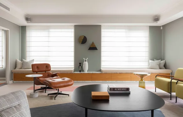 Modern living room with a brown leather chair, books on black coffee table, and large windows with blinds.