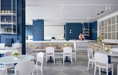 Modern cafe interior with blue walls, white chairs, and a staff member behind the counter.
