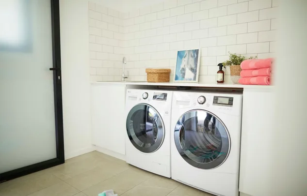 Modern laundry room with white washer and dryer, pink towels, wicker basket, and potted plant on counter.
