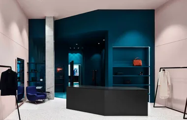Minimalist interior of a modern clothing store with dark teal walls, a counter, and displayed garments and accessories.