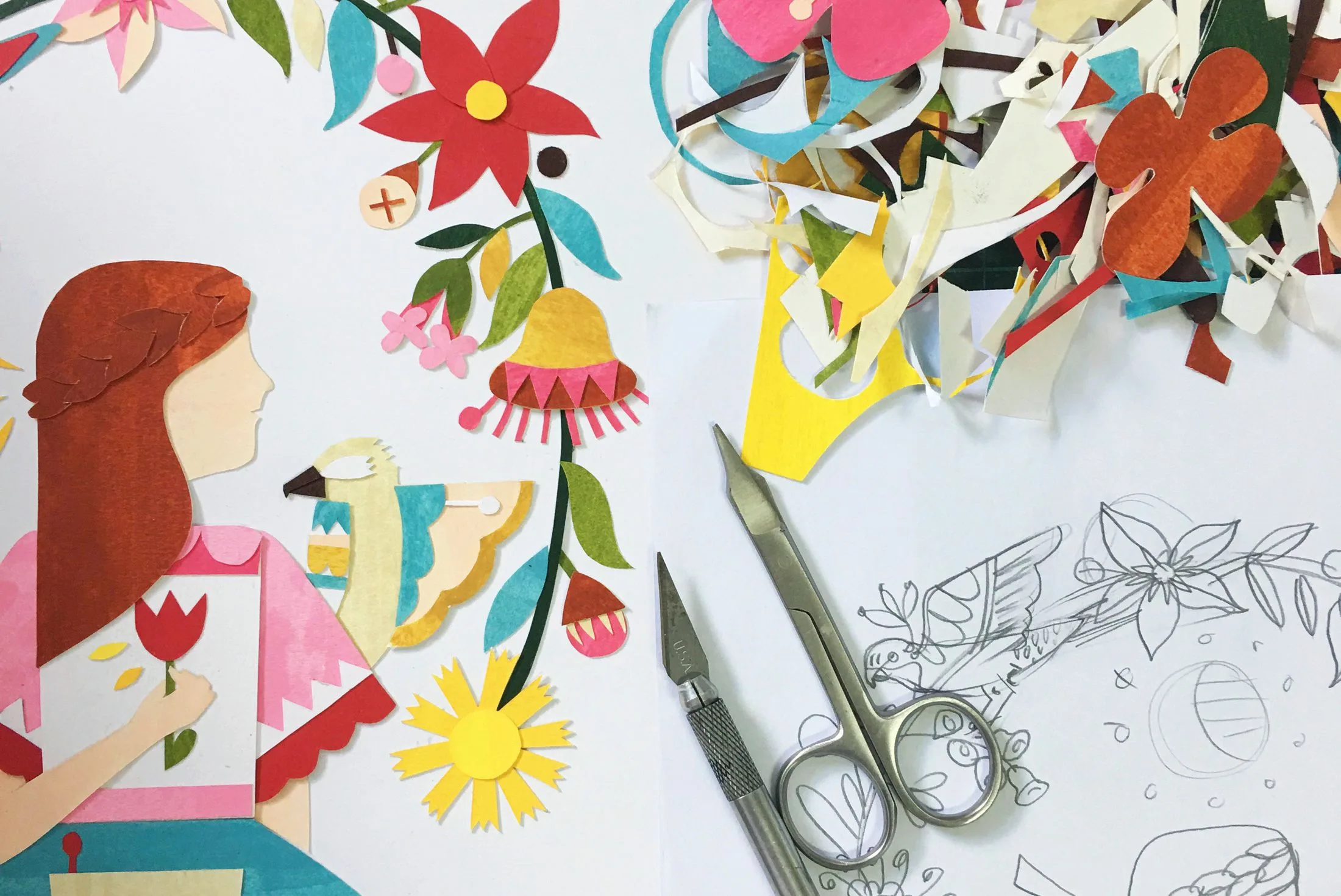 Collage art of a girl holding a flower with bird, colorful paper cutouts, scissors, and sketch on a table.