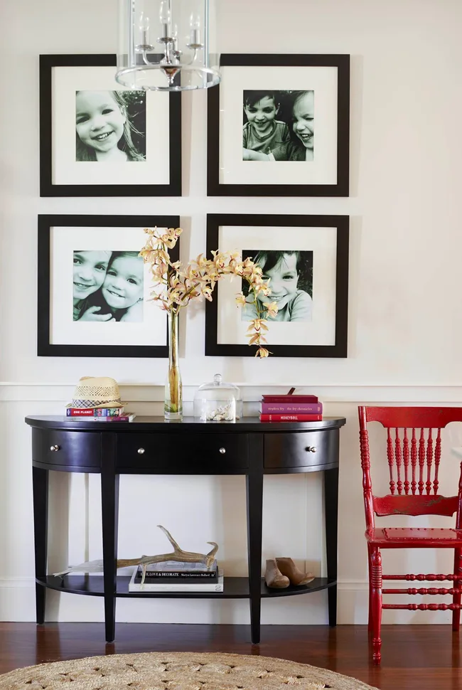 Console table with decor and photos of smiling kids. Red chair to the right, chandelier above.