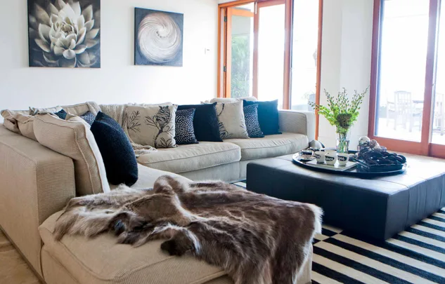 Bright living room with a beige sectional sofa, patterned cushions, cowhide throw, and a modern glass-topped coffee table.