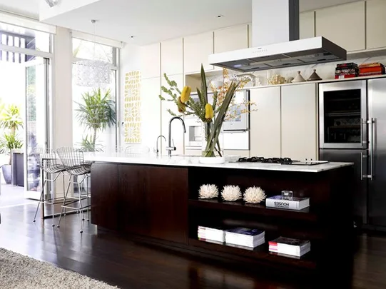 Modern kitchen with dark wood island, white countertops, stainless steel appliances, and large vase of flowers.