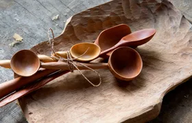 Hand-carved wooden spoons tied together with twine, resting on a carved wooden tray.
