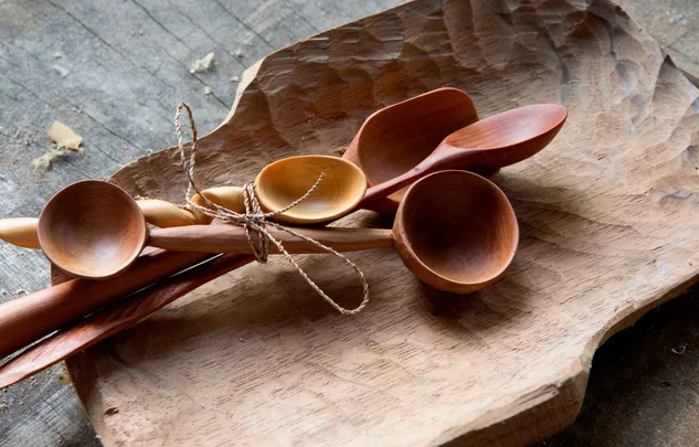 Hand-carved wooden spoons tied together with twine, resting on a carved wooden tray.