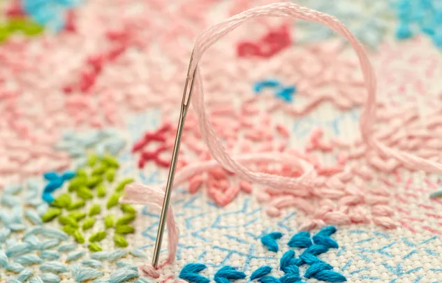 Needle with pink thread stitching colorful embroidery on fabric.