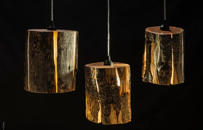 Three pendant lights made from split wood logs with glowing interior, set against a dark background.