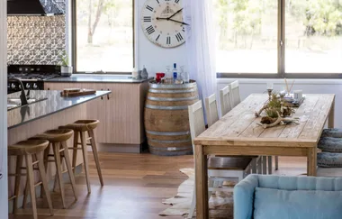 Modern kitchen and dining area with wooden stools, large clock, and table with decorative centerpiece.