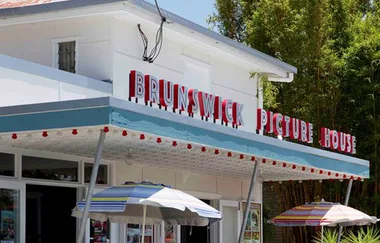 Brunswick Picture House exterior with retro signage, umbrellas, and green plants in the background on a sunny day.