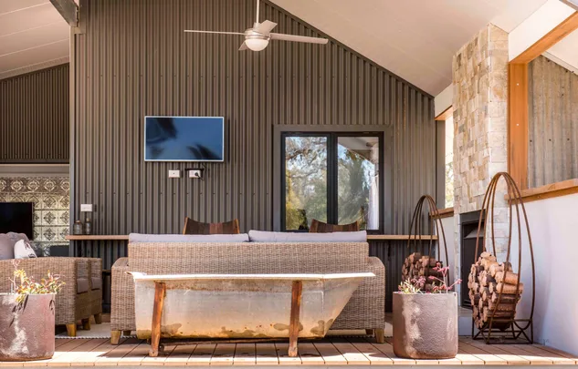 Outdoor patio with wicker furniture, a wall-mounted TV, firewood, and potted plants on a wooden deck.