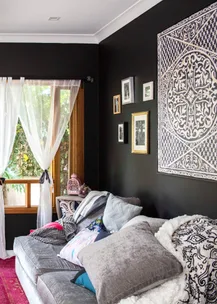 Cozy living room with gray sofa, colorful cushions, sheer curtains, and patterned wall art.