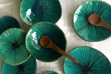 Green ceramic plates with black radial pattern, each with a wooden spoon, arranged on a textured white cloth.