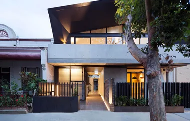 Modern two-story house with a geometric facade, large windows, and a tree in the foreground.