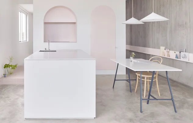 Modern minimalist kitchen with white island, wooden chair, and pendant lights; sleek and clean design.