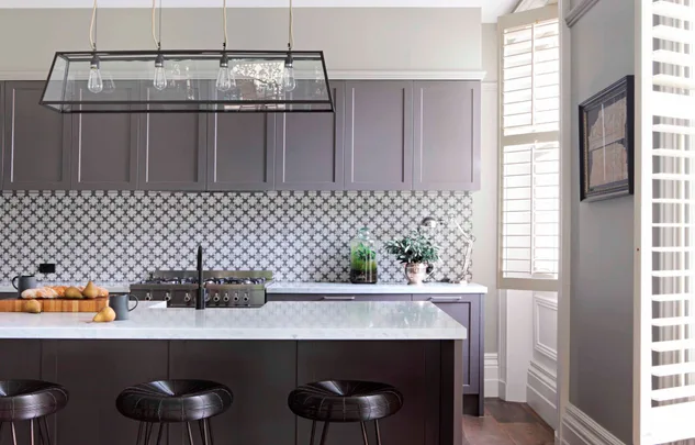 Modern kitchen with dark cabinets, patterned backsplash, hanging lights, and a white island with stools.