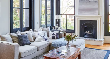 Living room with beige sofa, decorative pillows, glass coffee table, black-framed windows, and a fireplace.