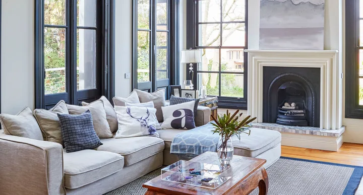 Living room with beige sofa, decorative pillows, glass coffee table, black-framed windows, and a fireplace.