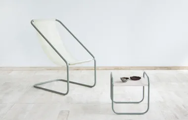 A minimalist sling chair and low table with pottery on a light stone floor.