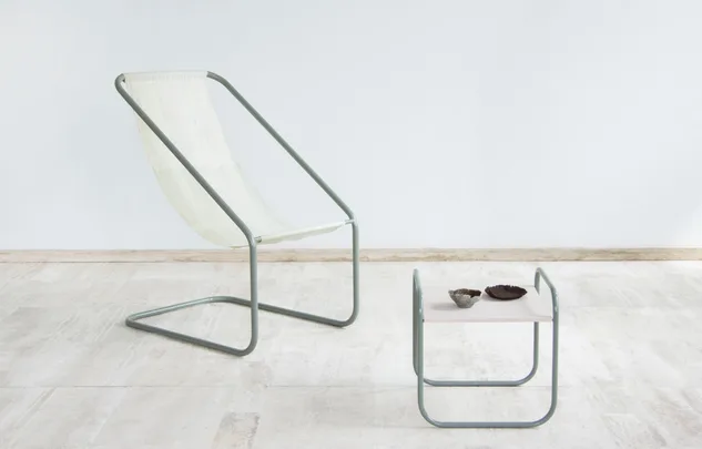 A minimalist sling chair and low table with pottery on a light stone floor.