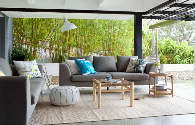 Outdoor living room with gray sofas, colorful cushions, a white pouf, and bamboo plants in the background.