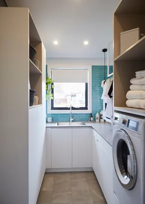 Modern laundry room with teal tiles, a large window, and a washing machine.
