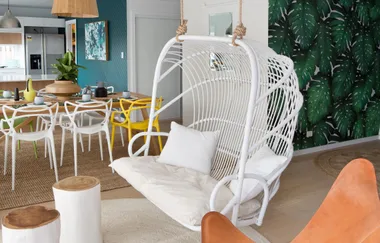 Bright living room with a white hanging chair, green leaf wallpaper, and a colorful dining area.