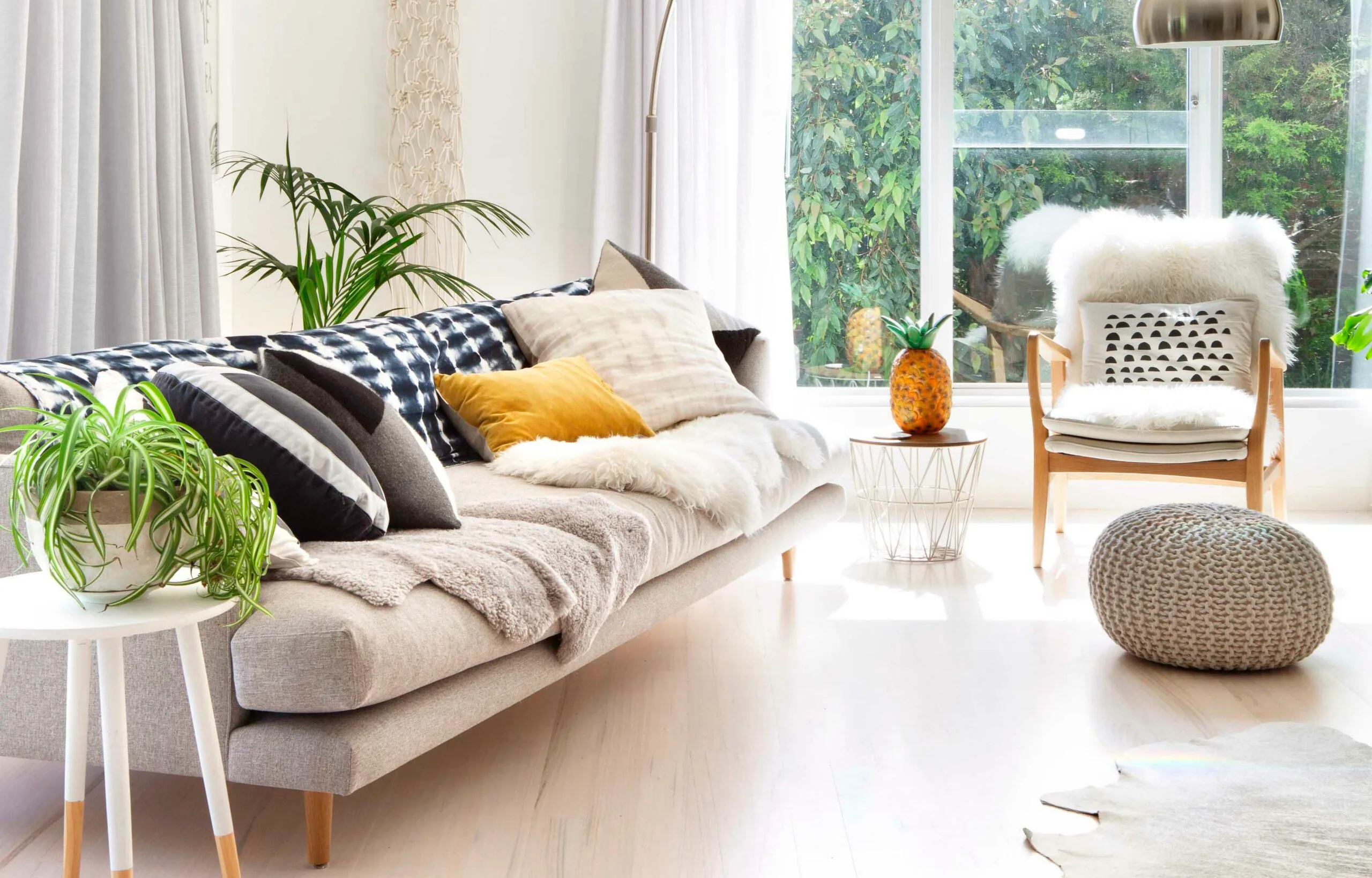 Bright living room with a beige sofa, various pillows, plant decor, and a pineapple-shaped lamp near a large window.