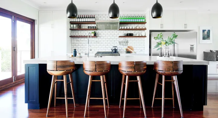 Modern kitchen with wooden stools, subway tile backsplash, and pendant lights over a central island.