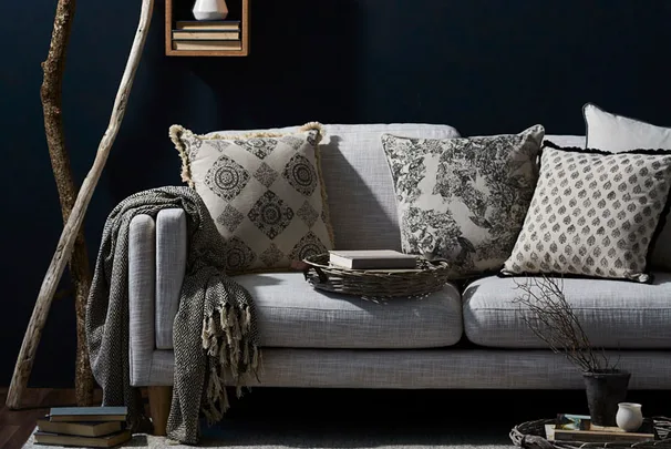 Cozy living room with a light gray sofa, patterned pillows, draped blanket, and books against a dark wall.