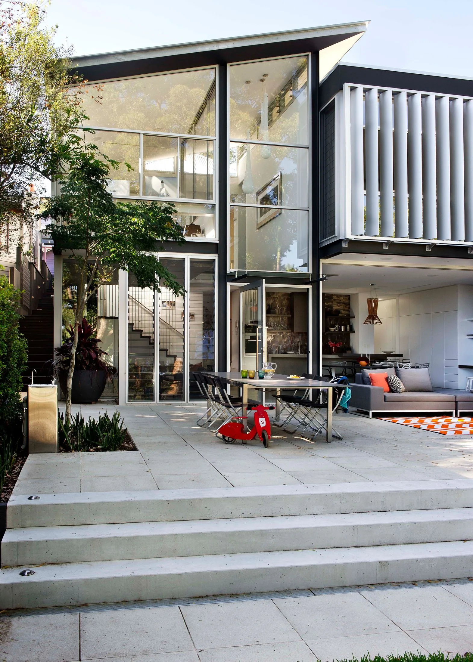 Modern house with large glass windows, patio with furniture, and a red scooter on the terrace.