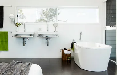 Modern bathroom with dual sinks, freestanding tub, green towel, and window view.