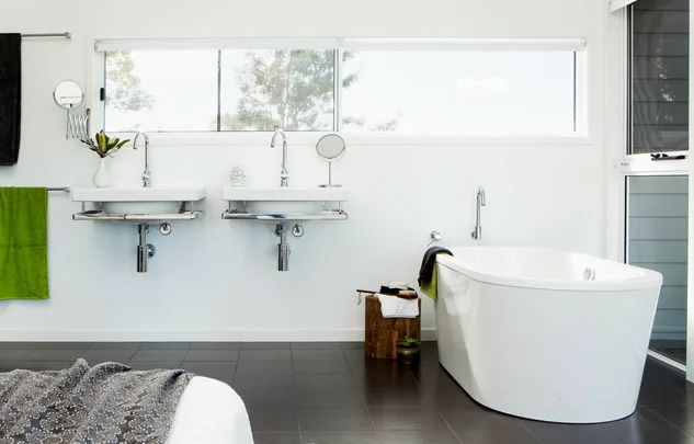 Modern bathroom with dual sinks, freestanding tub, green towel, and window view.