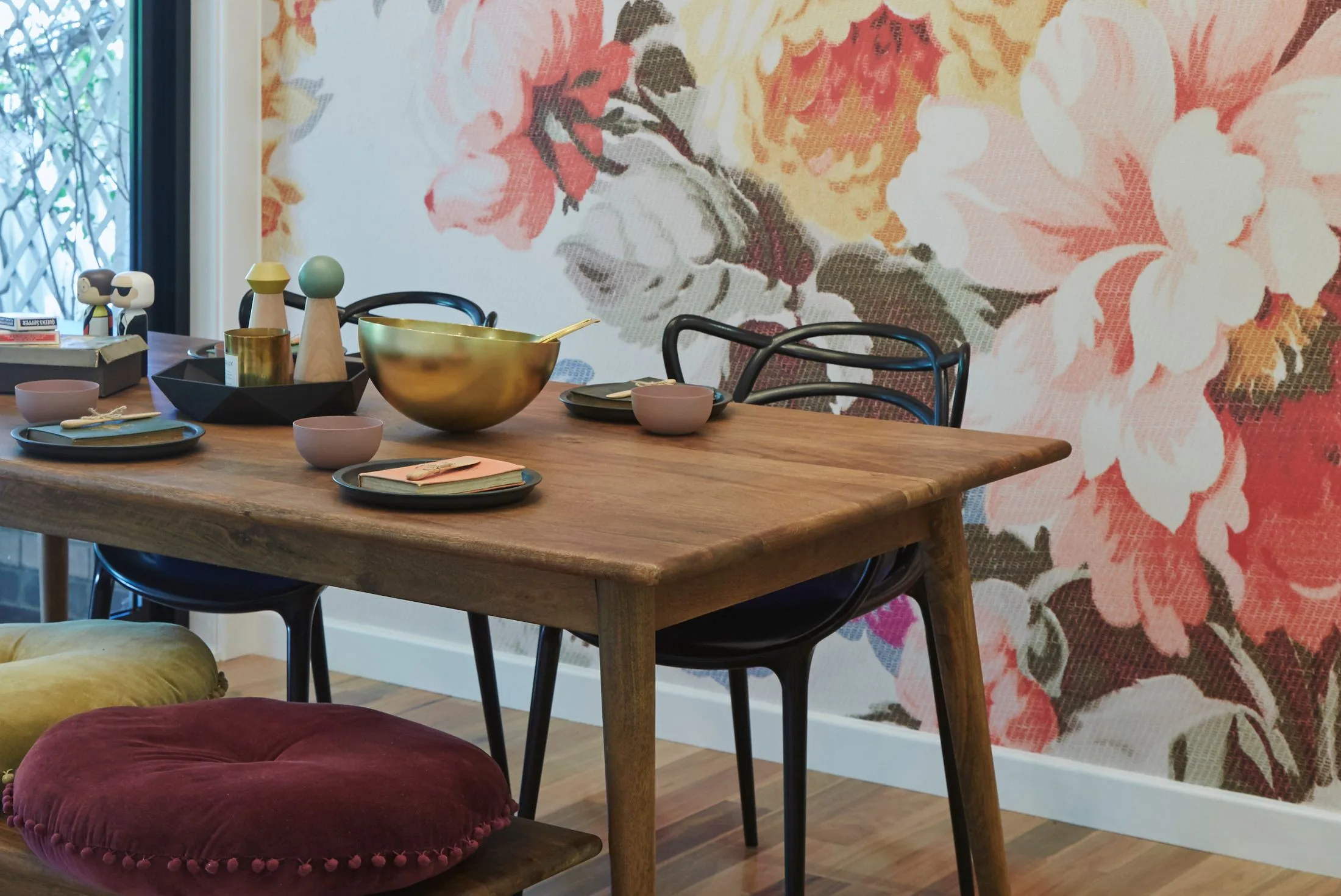 Dining table with decorative items, floral wallpaper, colorful cushions, and modern chairs.