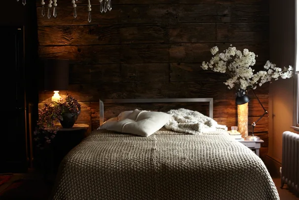 Cozy bedroom with wood-paneled wall, neutral bedding, bedside lamps, and floral arrangements enhancing the warm ambiance.