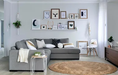 Modern living room with a gray sectional sofa, decorative cushions, wall art, and a round jute rug on a wooden floor.