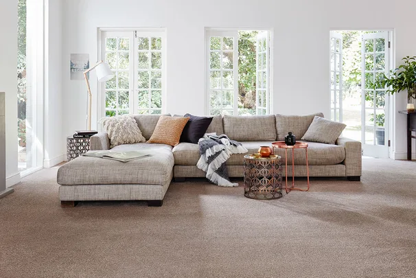 Cozy living room with a gray sectional sofa, cushions, throw blanket, and large windows overlooking a garden.