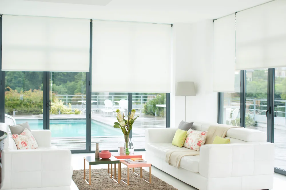 Bright modern living room with white furniture, glass walls, and outdoor pool view.