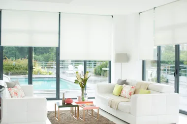 Bright modern living room with white furniture, glass walls, and outdoor pool view.