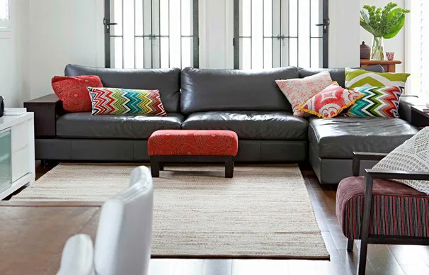Large black leather sofa with colorful patterned cushions in a bright living room.