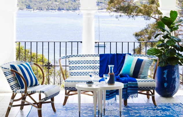 Outdoor seating with blue-striped cushions, table, and potted plant on a balcony overlooking a serene lake view.